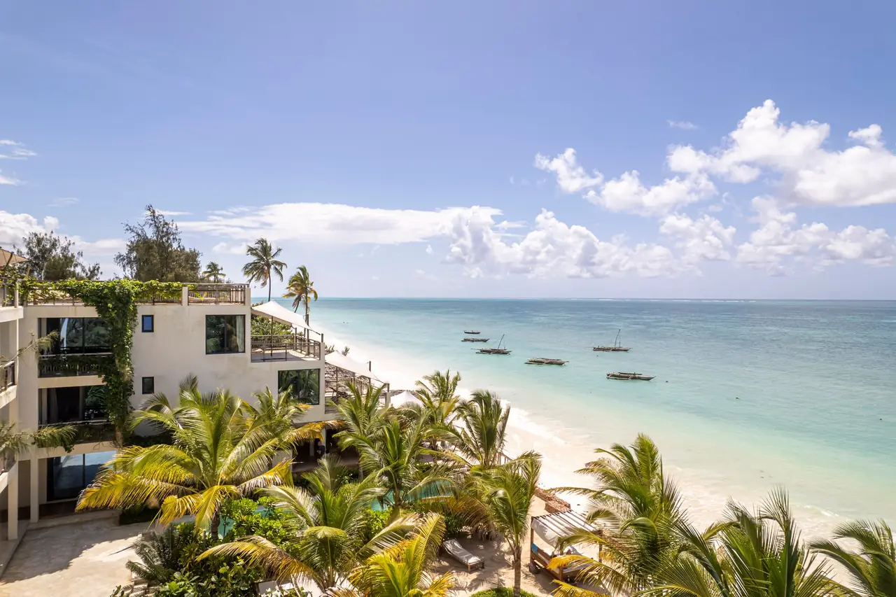 Aerial view of the hotel's white buildings among palms, right above Jambiani's beach and turquoise lagoon