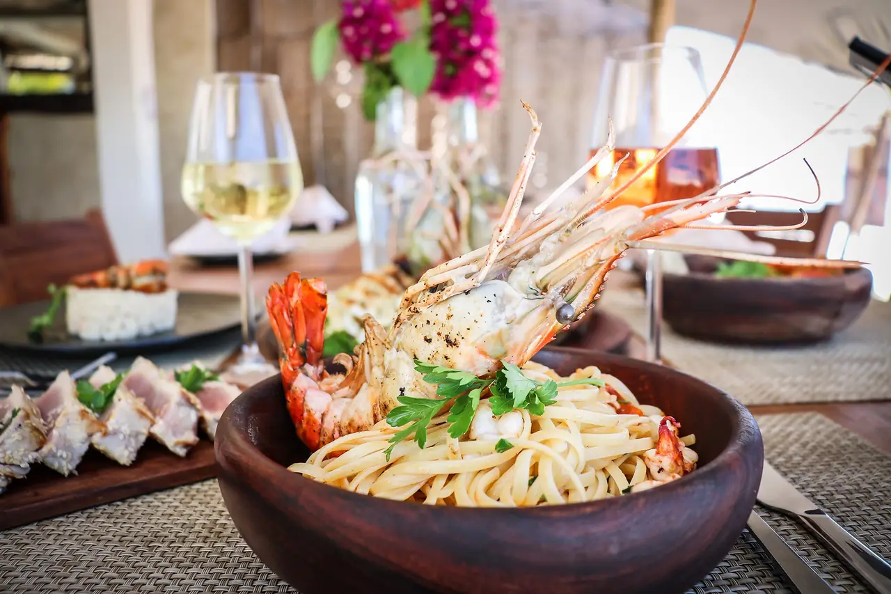 Seafood pasta with grilled prawns and a glass of white wine on the restaurant table