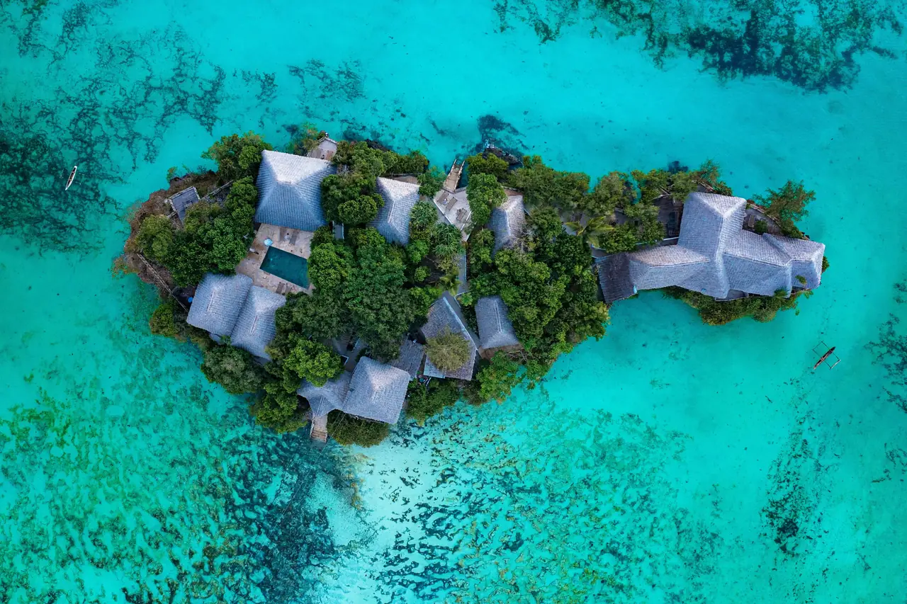 Aerial view of the tiny coral island and its thatched villas, surrounded by turquoise sea