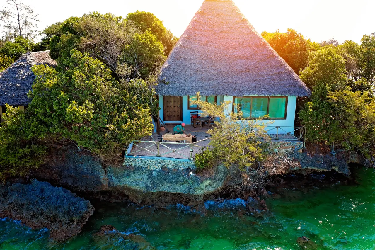 A thatched villa perched on coral rock above the water