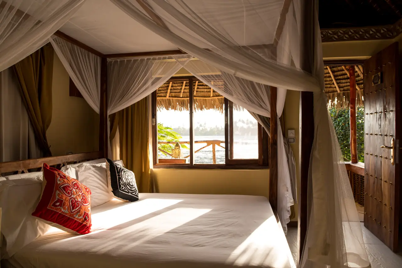 A villa bedroom with a draped bed and a window to the sea