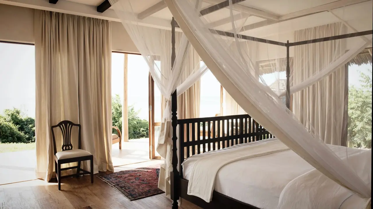 A four-poster bed with white nets and garden views