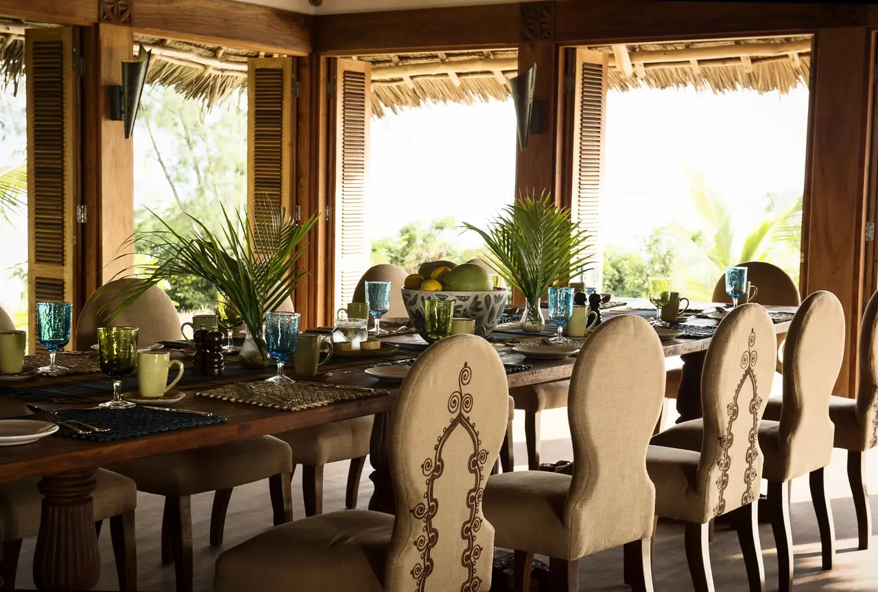 A long dining table set under a thatched roof