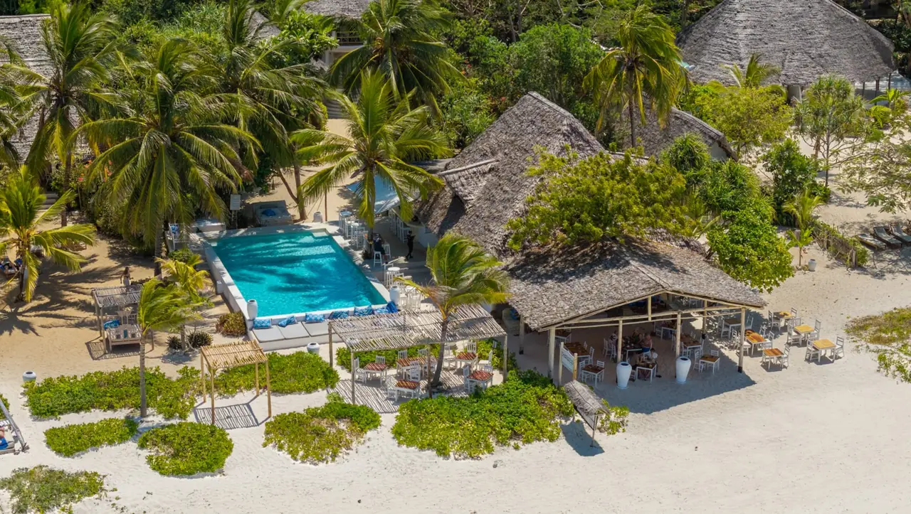 Aerial view of thatched buildings, a pool and palms on Jambiani's beach