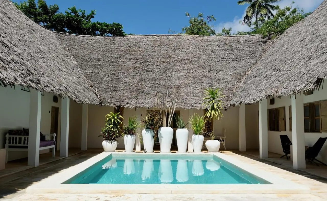 A small pool in a courtyard of thatched, white-columned buildings