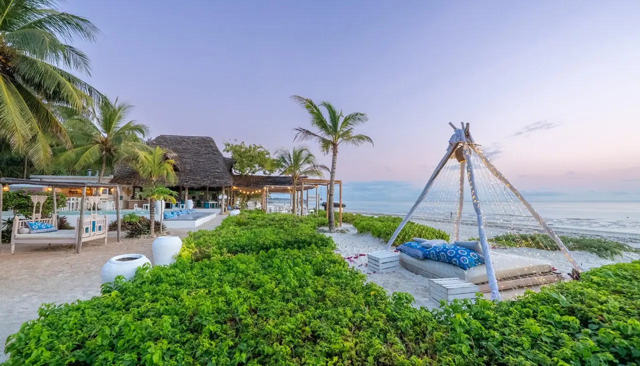 A rope swing and day beds in a garden above the beach at dusk