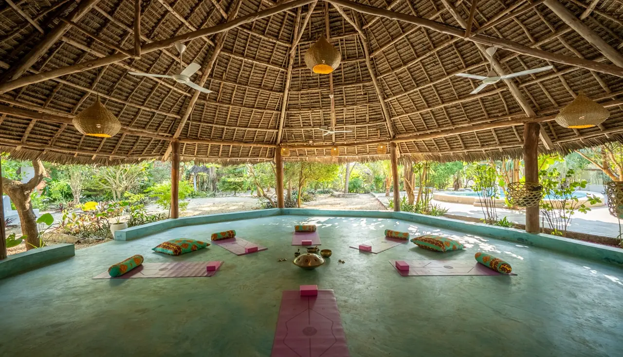 An open-sided thatched yoga shala with mats laid out