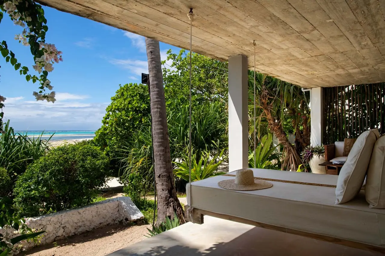 A shaded daybed terrace under palms overlooking the beach