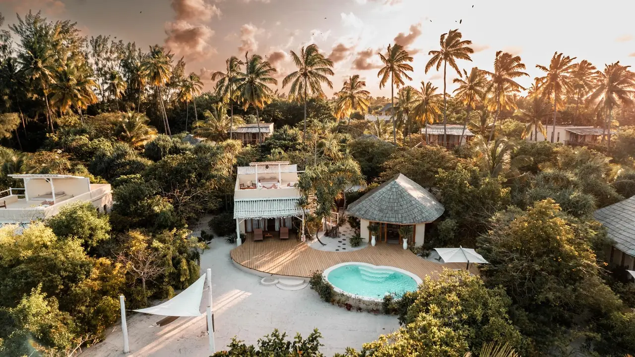 Aerial view of a villa and its round pool among palms in evening light