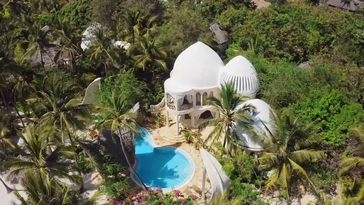 Aerial view of a white domed villa with a curved private pool among trees
