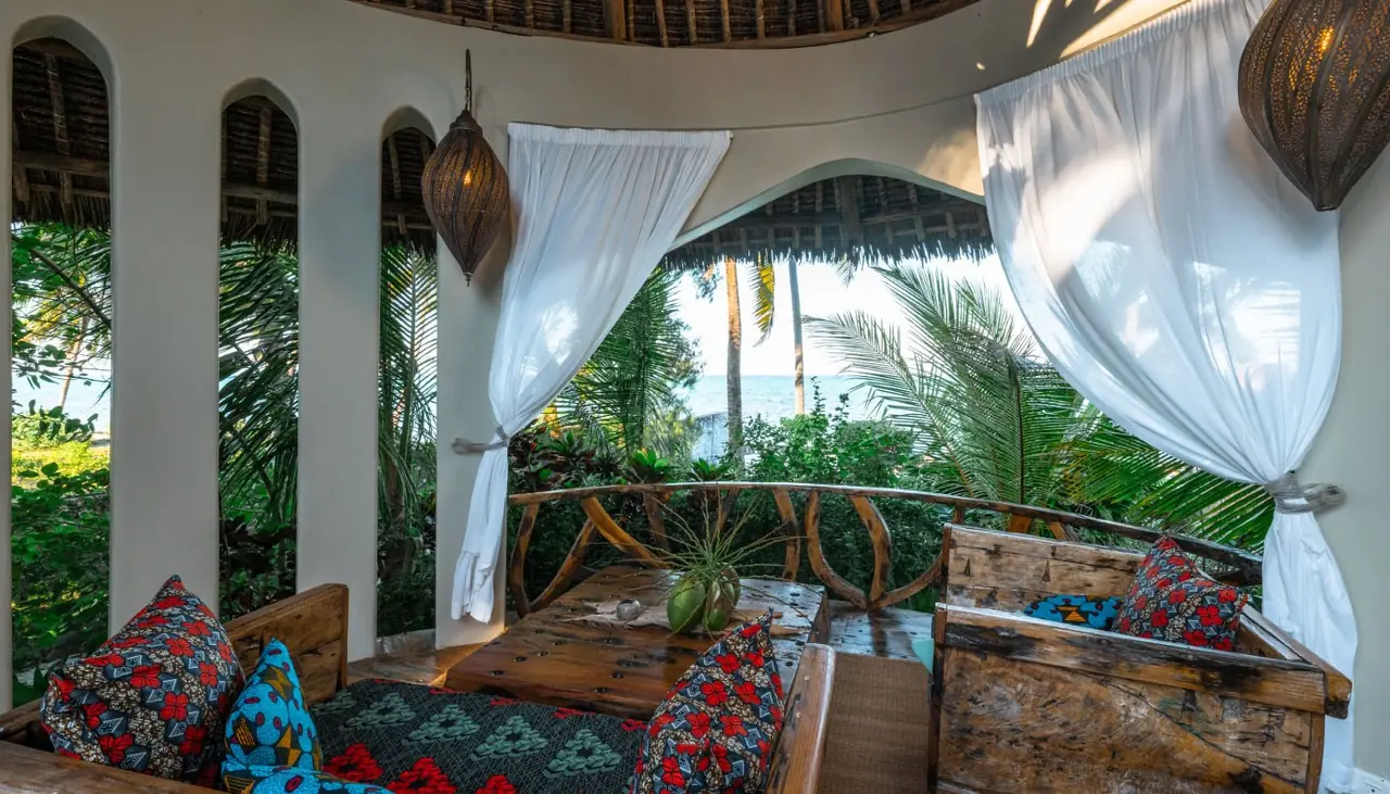 An open-sided lounge with arches, cushions and garden views