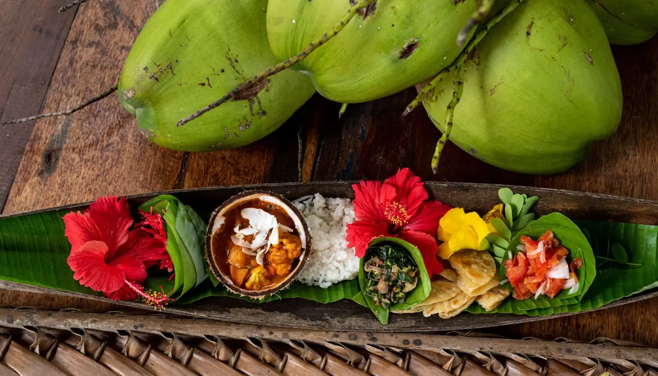 Colourful local dishes served on a banana leaf with hibiscus flowers and coconuts