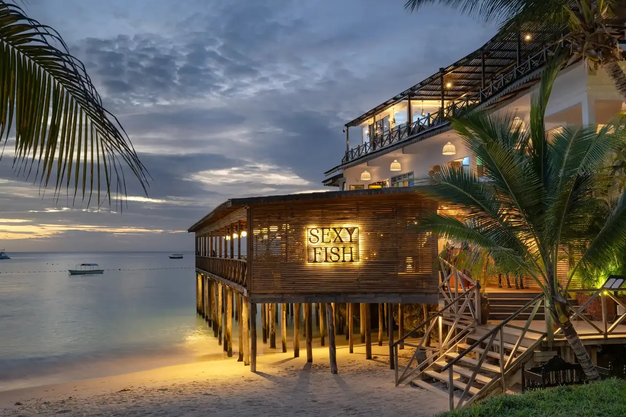 The stilted Sexy Fish restaurant lit up on the beach at dusk