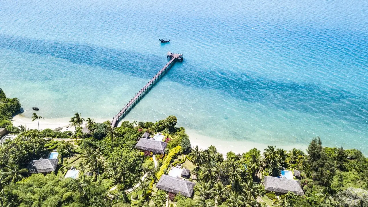 Aerial view of the long wooden jetty reaching out over turquoise water from the wooded shore