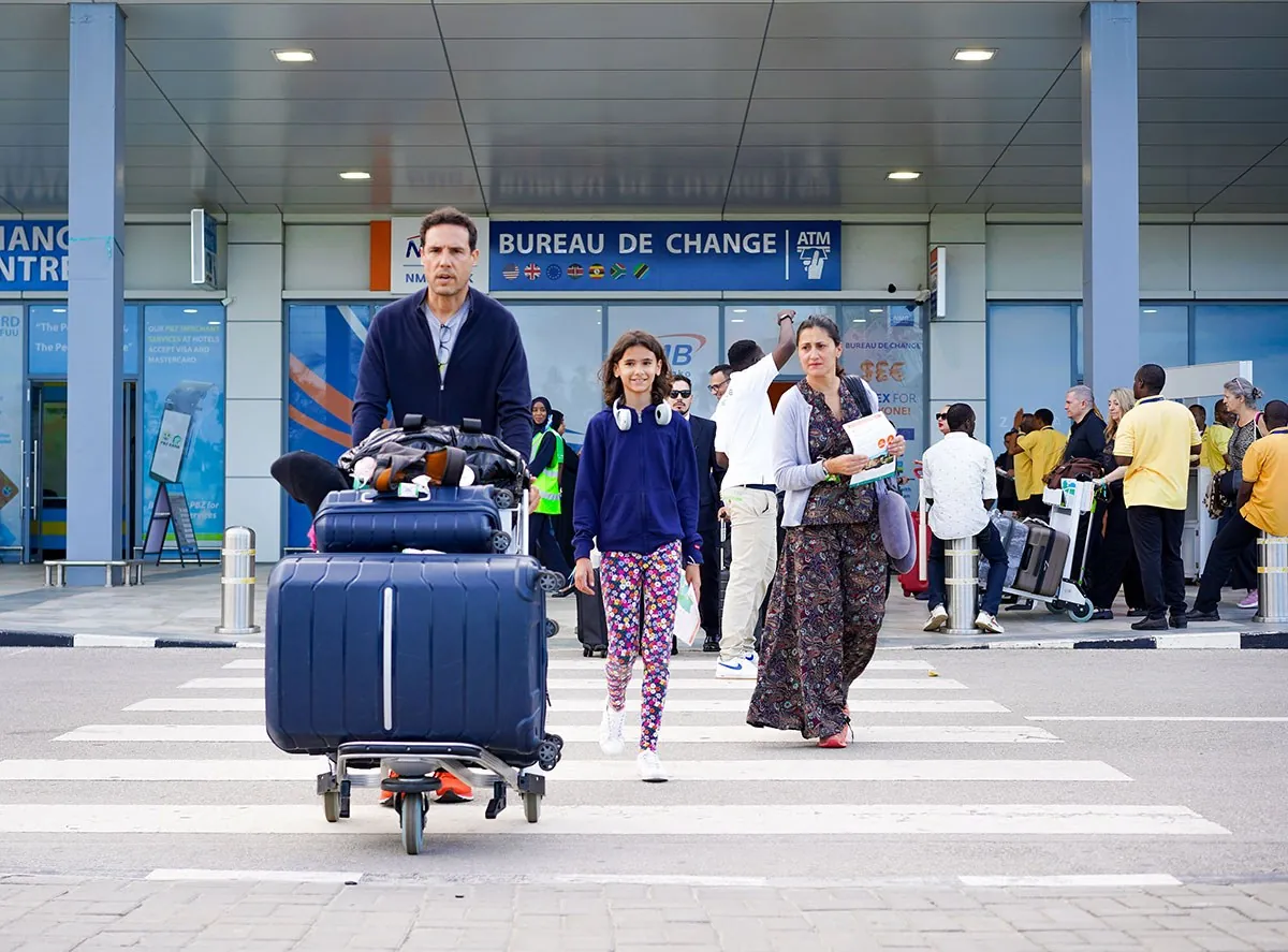 Passengers with a luggage trolley leaving the arrivals building, with Bureau de Change and ATM signs behind
