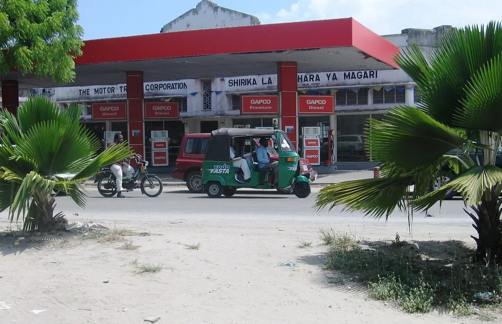 Green bajaji and a motorbike passing a fuel station