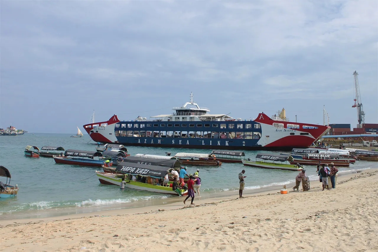 Tourists wading out to climb into a canopied wooden boat on Stone Town beach, with rows of similar trip boats and the Azam Sea Link 2 ferry behind