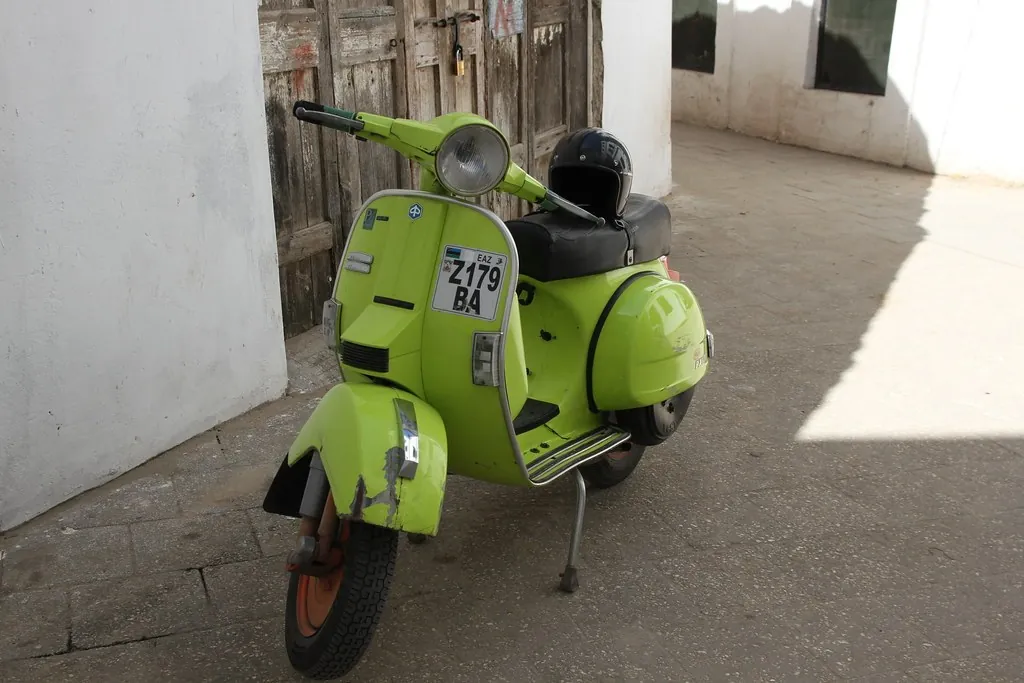 Lime-green Vespa with a helmet on the seat, parked in a narrow lane