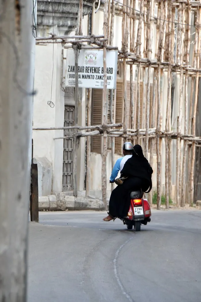 Woman riding side-saddle as a pillion passenger on a scooter in a Stone Town street