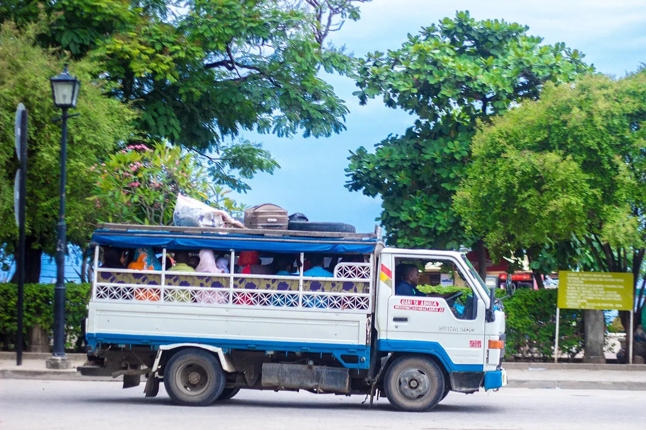 Blue and white dala dala truck with open sides and luggage on the roof