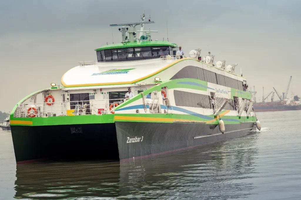 Green, white and black catamaran Zanzibar 3 with crew on deck, in an industrial harbour