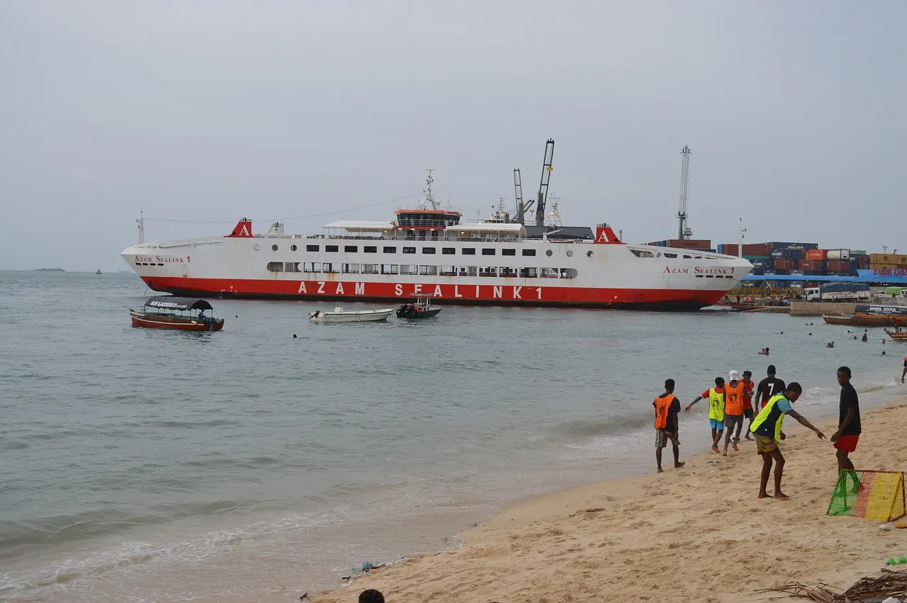 Large white-and-red ro-ro ship Azam Sealink 1 at the Zanzibar port, seen from Stone Town beach where young men play football