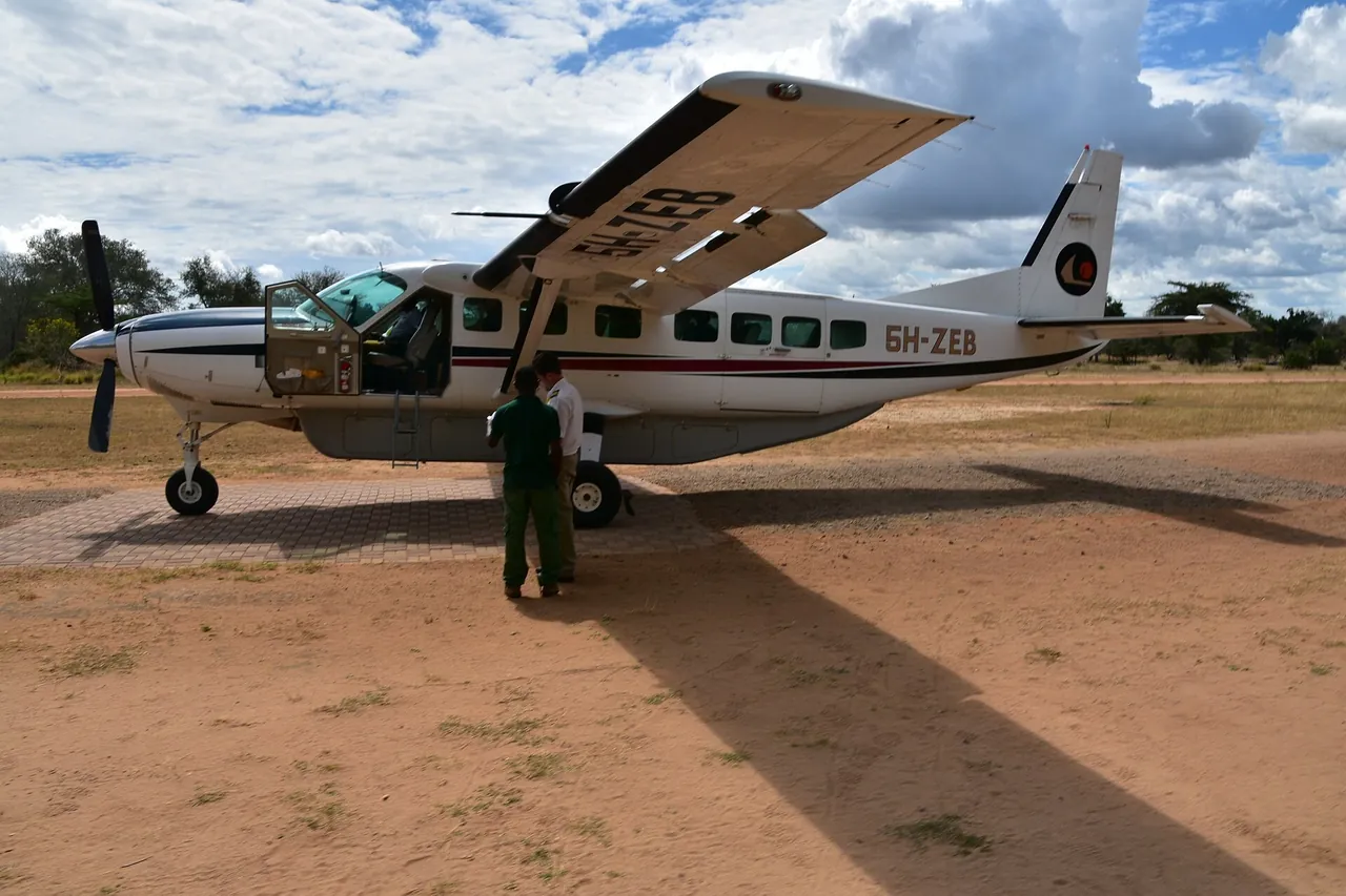 Coastal Aviation Cessna Caravan 5H-ZEB parked on a red-earth bush airstrip with a pilot and ground staff beside it