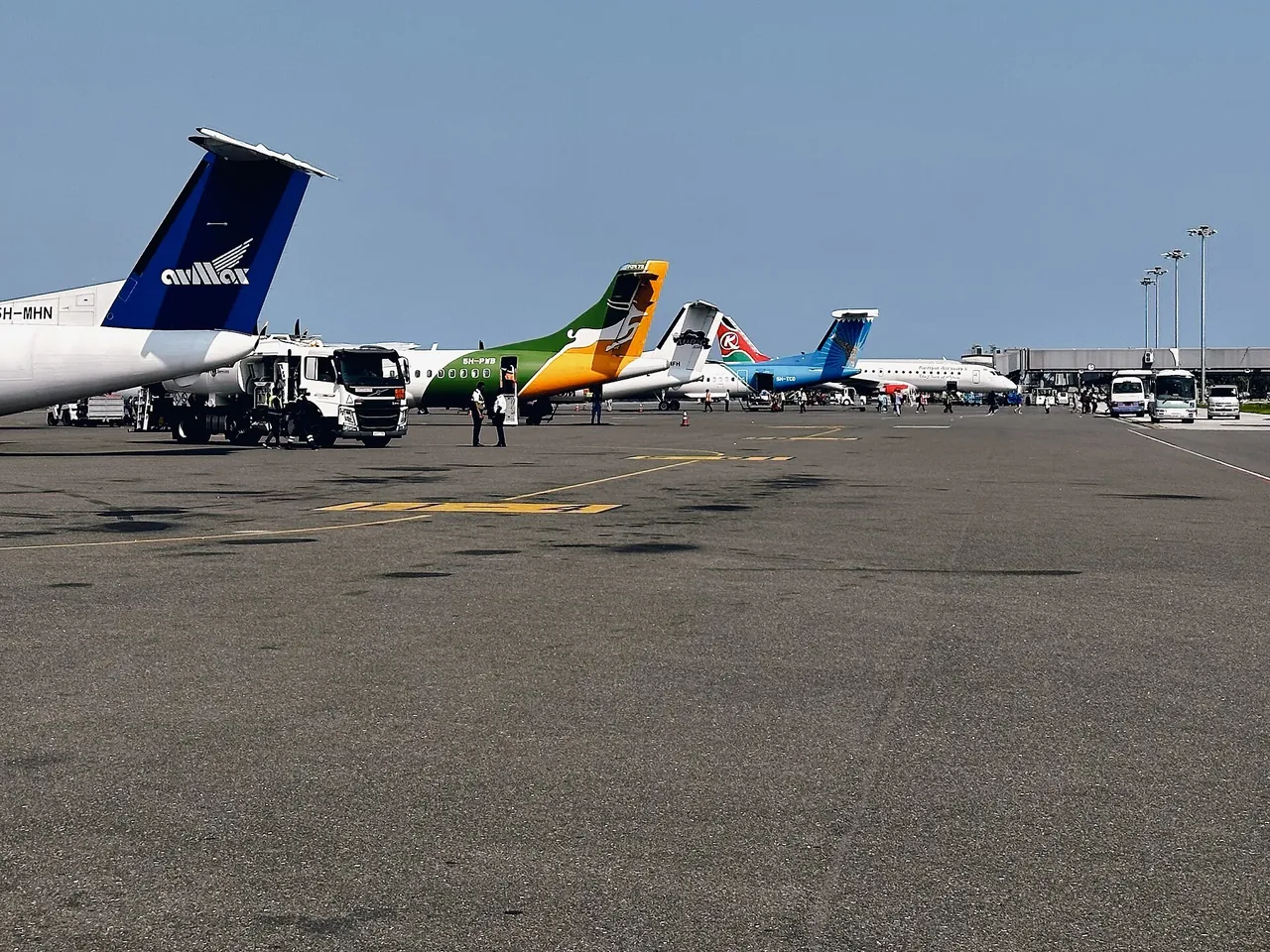 Apron at Zanzibar airport with the tails of several turboprops and a Kenya Airways jet lined up near the terminal