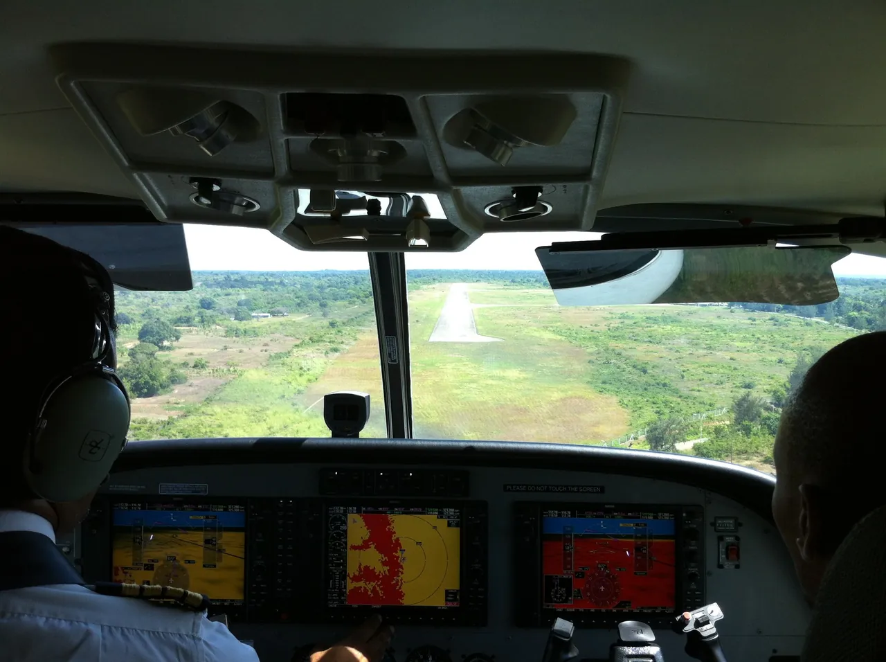 View from the cockpit of a small plane on final approach to a single runway through green countryside