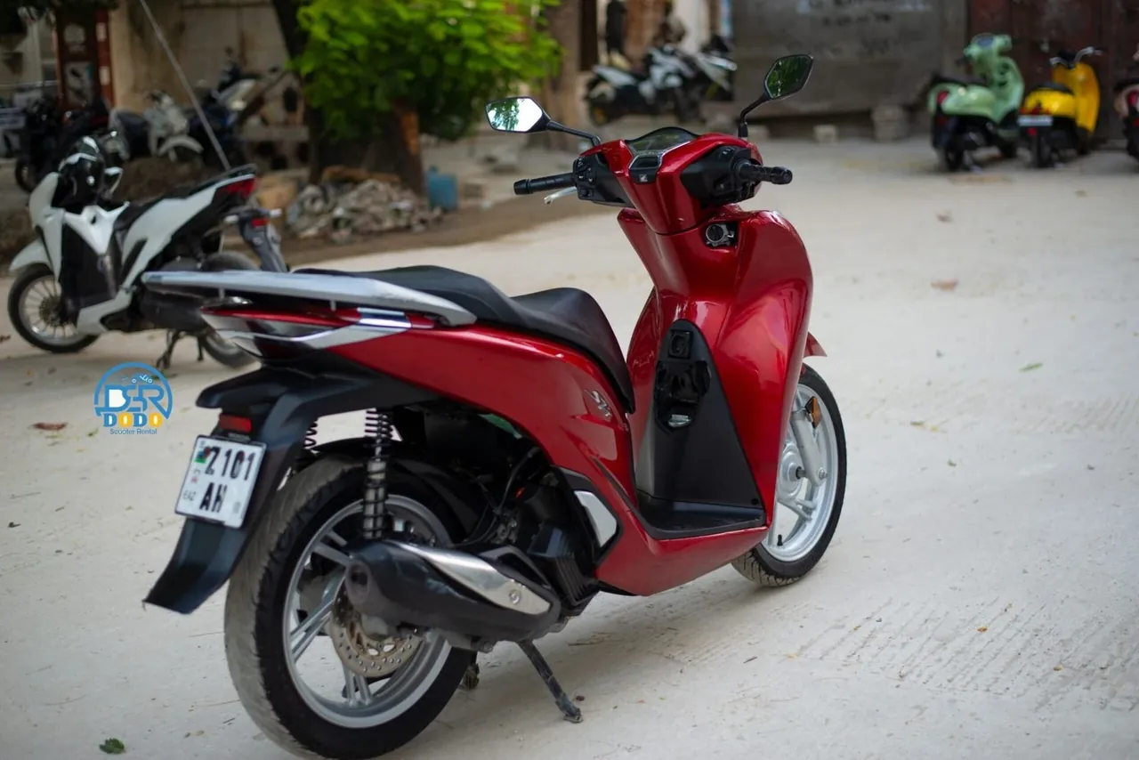 A red Honda SH scooter with a Zanzibar 'Z' number plate in a yard with other rental scooters behind