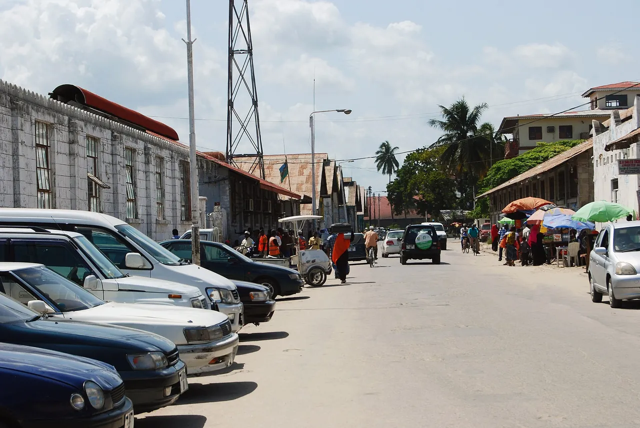 Street near the ferry terminal with parked cars, old port warehouses, porters in orange vests and umbrella stalls