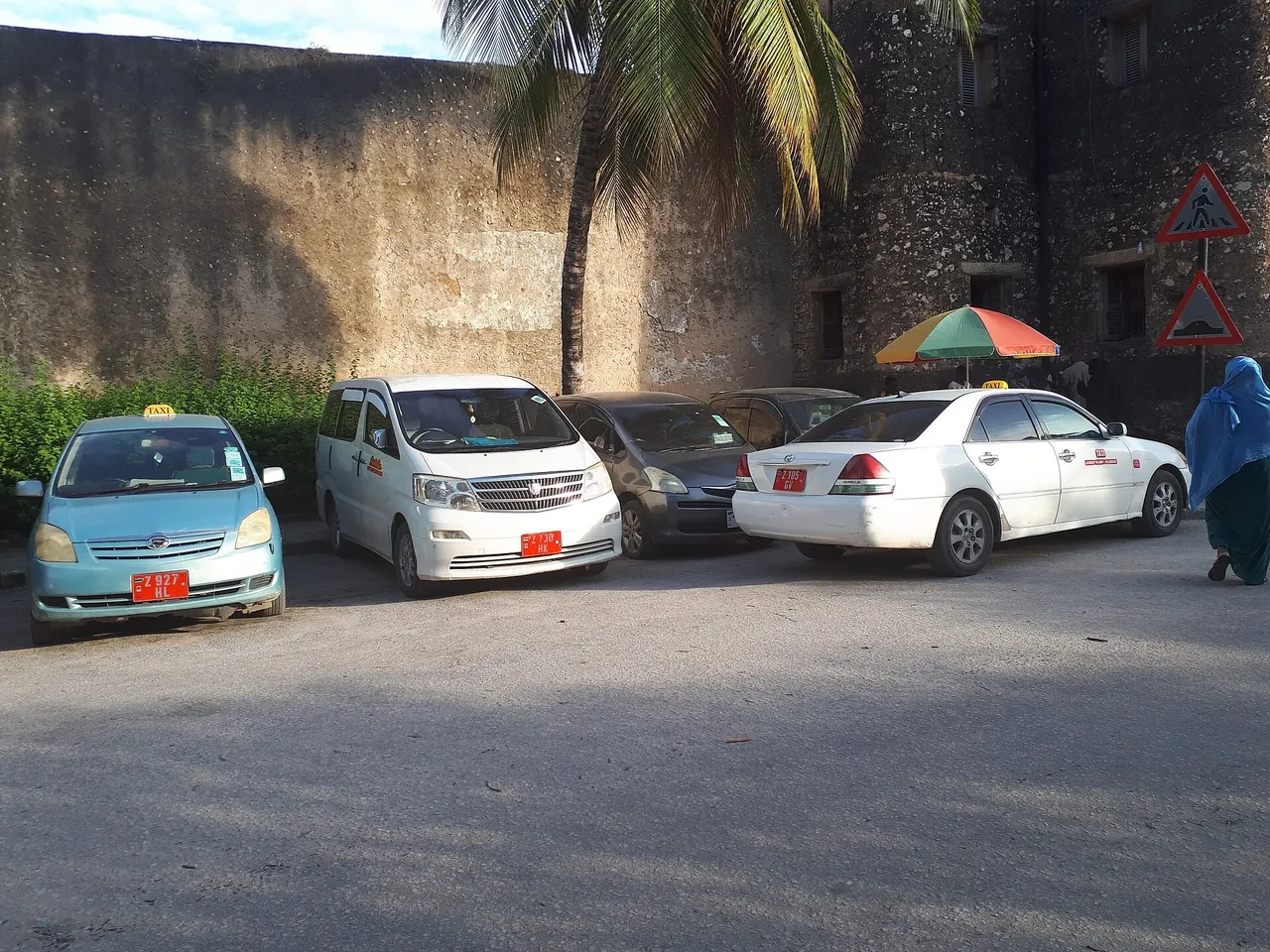Row of parked taxis with red number plates beside an old stone wall