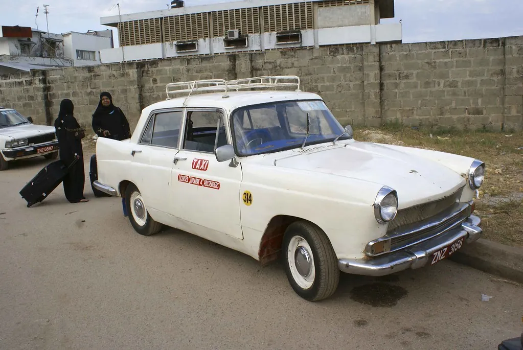 Old white saloon car marked TAXI with a roof rack