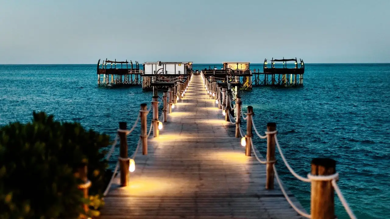 A lit wooden jetty leading over the sea to an overwater restaurant