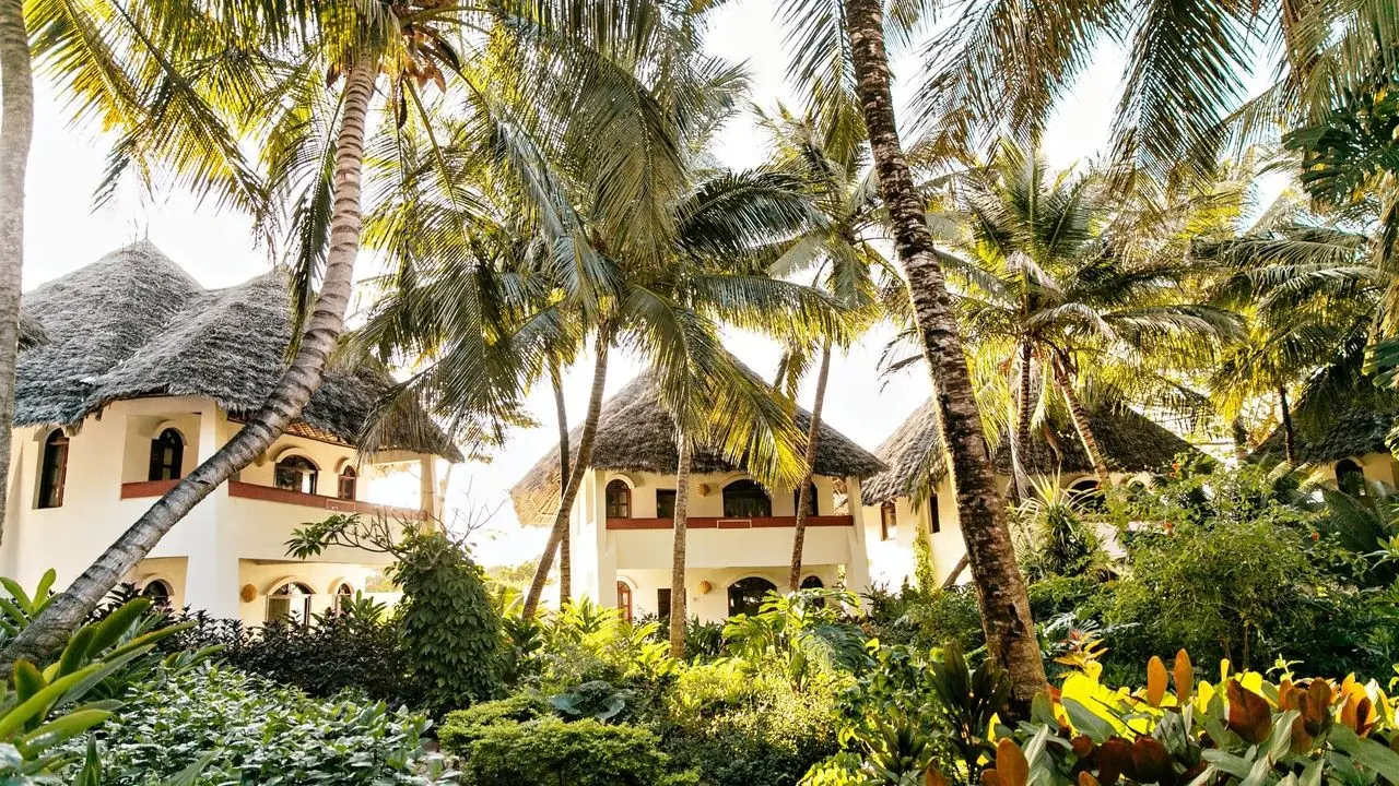 White suites with thatched roofs among palms and tropical gardens