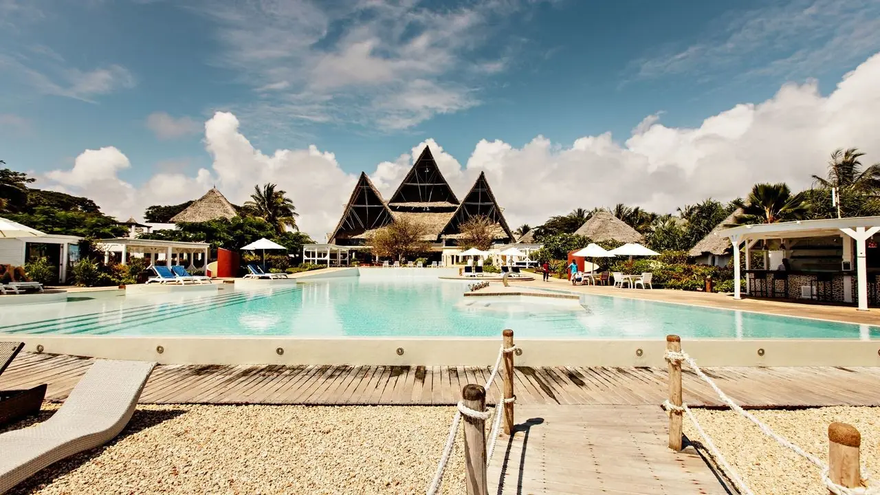 A pool in front of tall A-frame thatched roofs