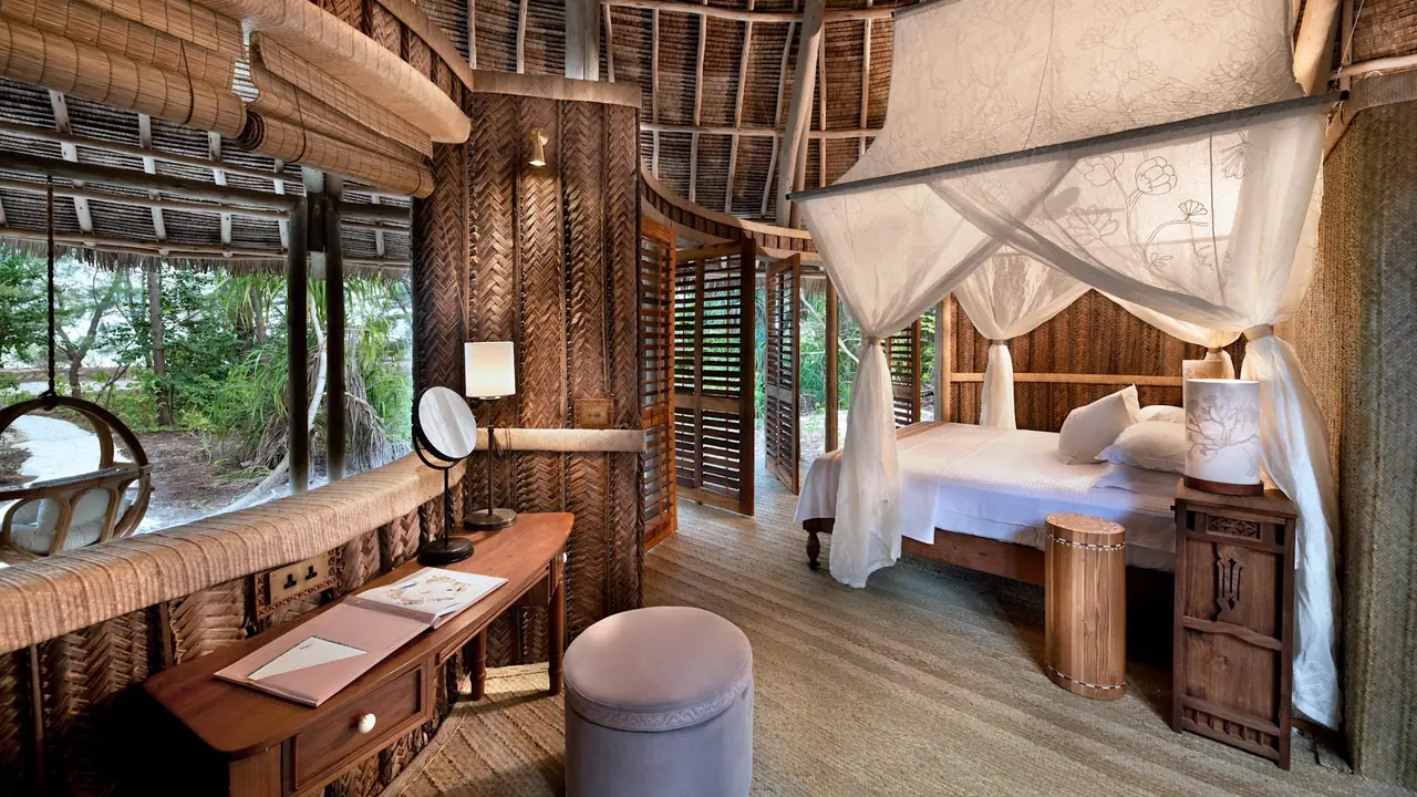 A banda bedroom with a draped bed, timber walls and louvred openings to the forest