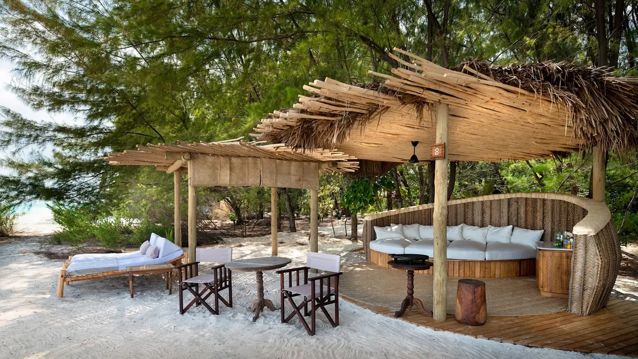 A shaded beach lounge with day beds on the sand at the edge of the forest