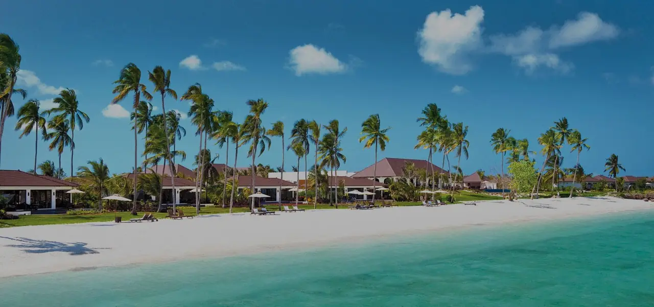 Low villas among palms behind a white beach and turquoise water
