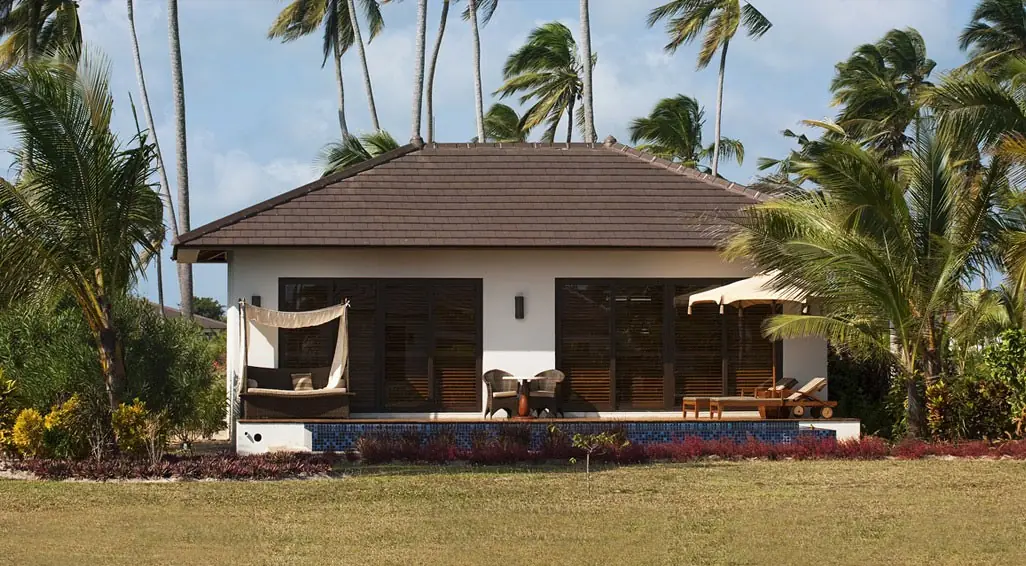 A white villa with a dark roof, terrace and private pool in a palm garden