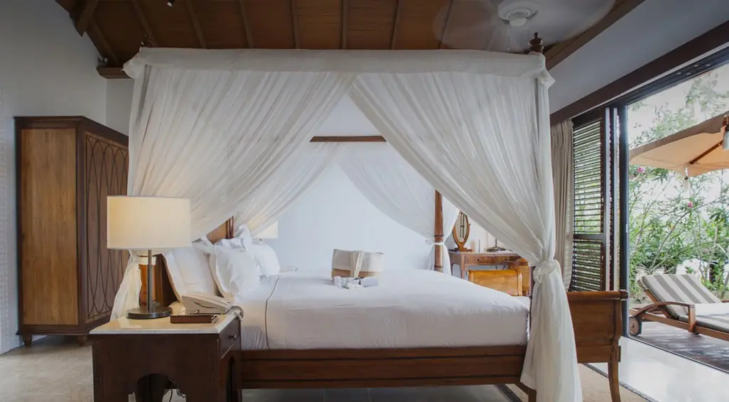 A villa bedroom with a white canopy bed and wooden shutters