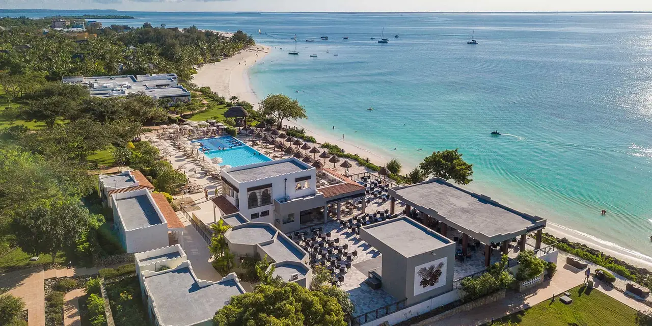 Aerial view of the resort buildings and pools beside a white beach and turquoise sea