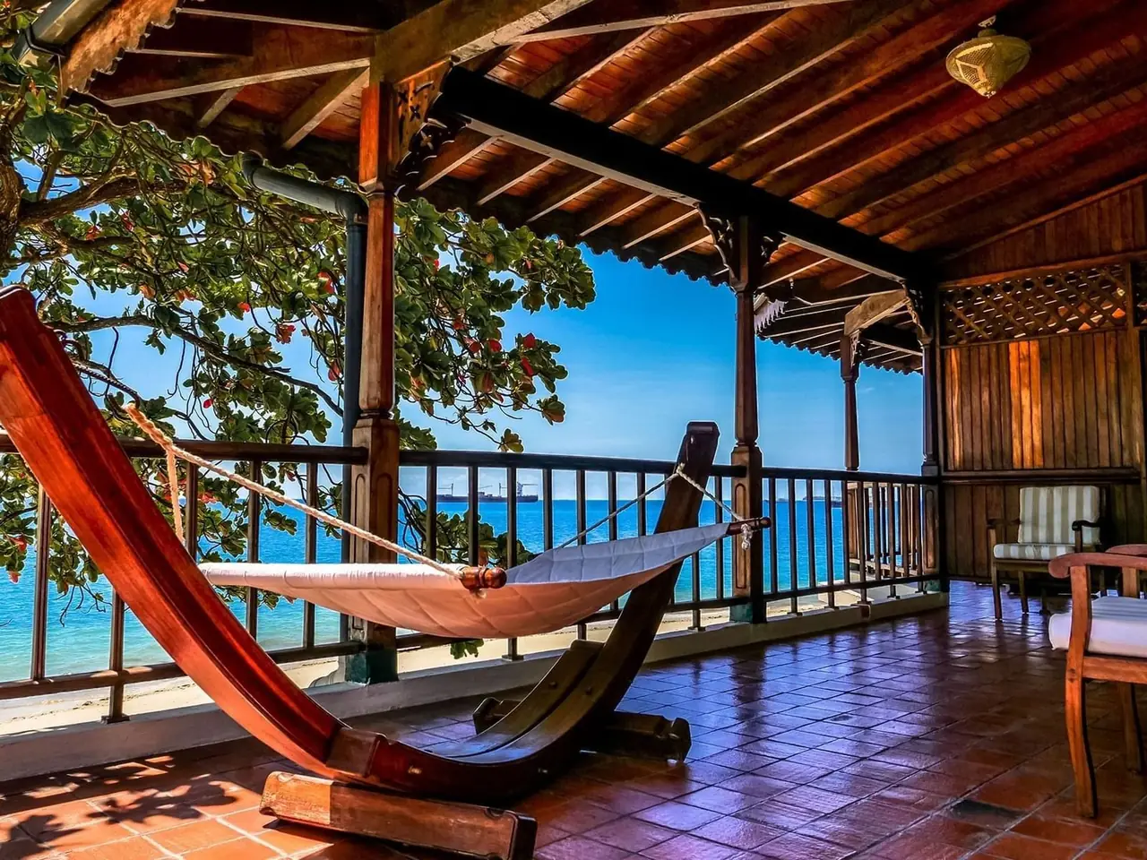 A covered veranda with a hammock and wooden balustrade looking out to sea