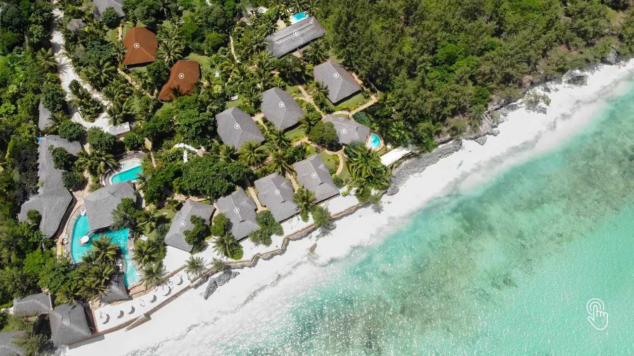 Aerial view of thatched villas, pools and gardens above a white beach