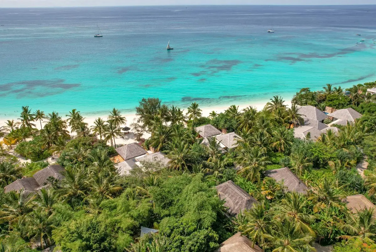Aerial view of thatched bungalows in tropical gardens above Kendwa's white beach and turquoise sea