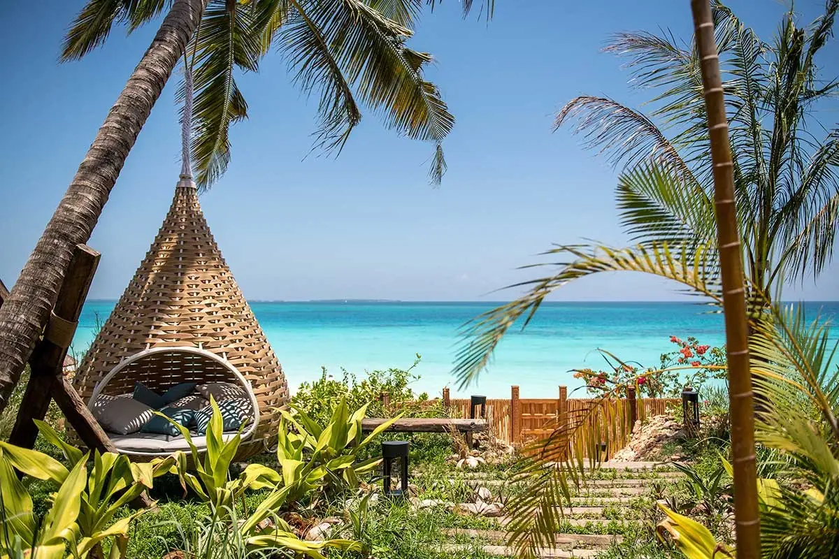 A woven nest-shaped day bed among palms, looking out to a turquoise sea