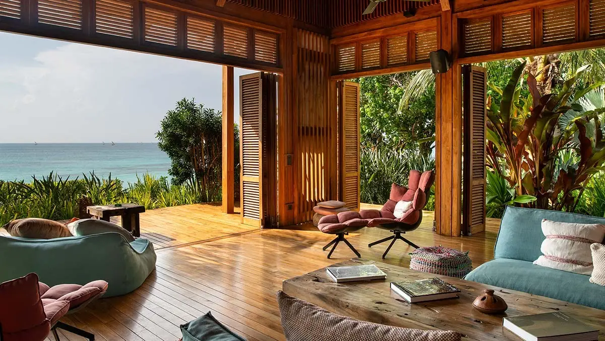 An open timber living room with sofas and wide doors onto the garden and sea