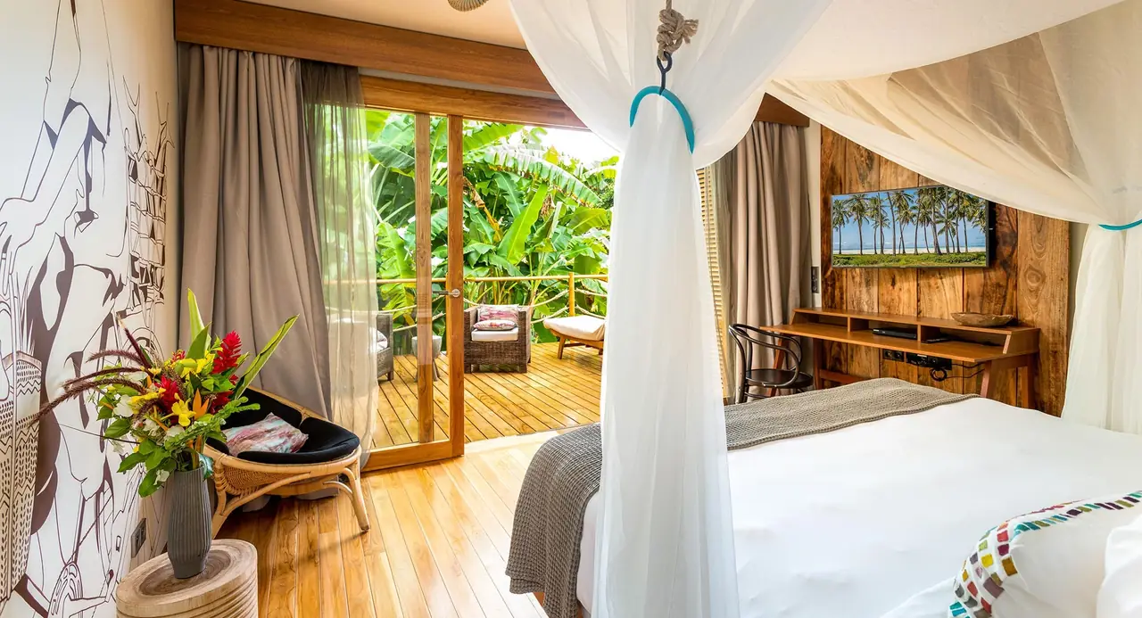 A bedroom with a draped bed and a timber deck looking into the garden