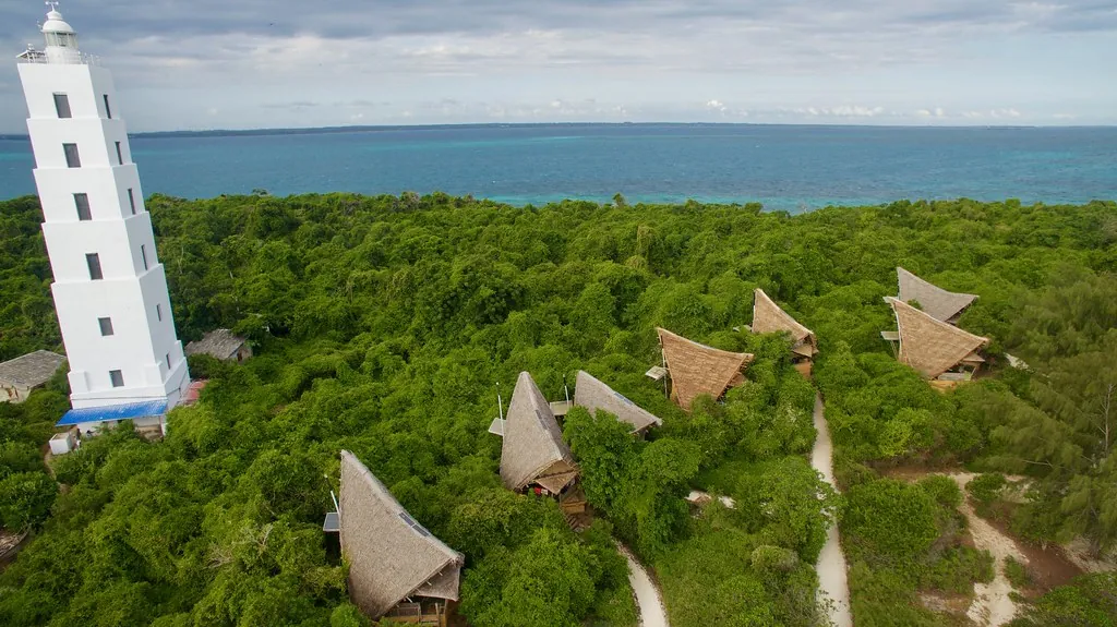 Aerial view of the white lighthouse and the thatched eco-bungalows among dense green forest