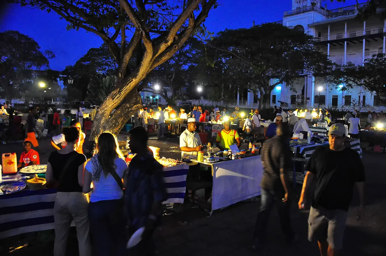 The Forodhani night food market under trees, lit by lamps, with people browsing the stalls